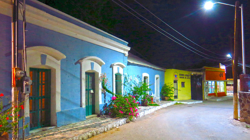 It's colorful. I see a couple street lights and utility poles. There's a few buginvillas in front of the blue building. The orange building is a mercado, open for business. ADA sidewalks.